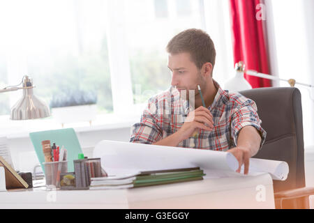 Architetto focalizzato con blueprint lavora al computer portatile in ufficio Foto Stock