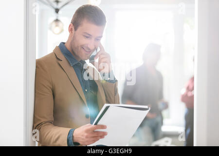 Imprenditore sorridente parlando al cellulare e guardando verso il basso in corrispondenza di notebook in ufficio Foto Stock