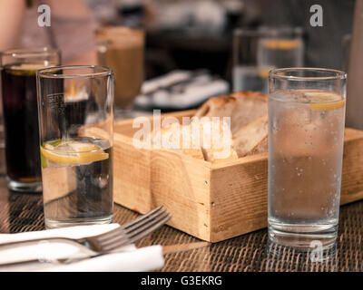 Scatola di pane appena sfornato di pane croccante con bicchieri di acqua con le fette di limone sulla messa in tavola con n. di persone Foto Stock