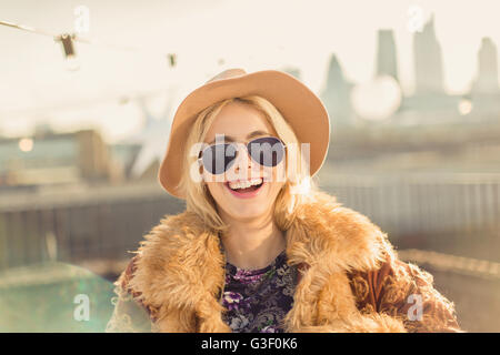 Ritratto entusiasta giovane donna che indossa un cappello e occhiali da sole sulla soleggiata terrazza sul tetto Foto Stock