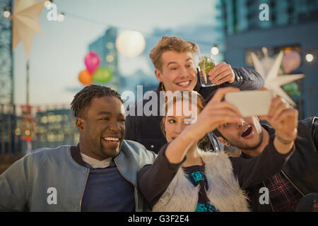 Giovani amici adulti tenendo selfie al partito sul tetto Foto Stock