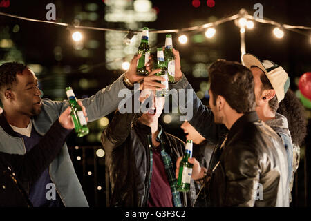 Giovani uomini la tostatura le bottiglie di birra in parte sul tetto Foto Stock