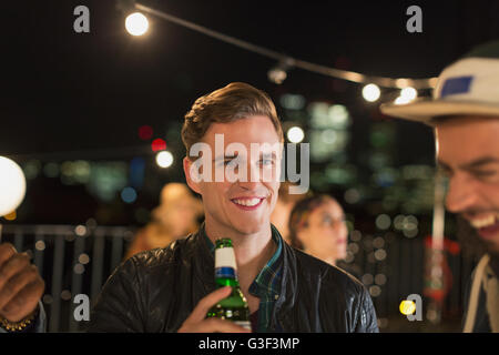 Sorridente giovane uomo di bere birra a parte sul tetto Foto Stock