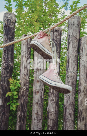 Sneakers appeso a una fune in giardino con travi in background. Foto Stock