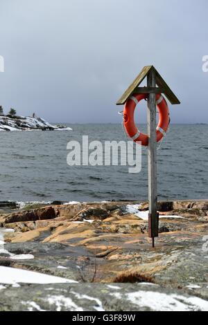 Anello di vita appesa su un supporto di legno. Costa rocciosa nella Finlandia meridionale, Porkkala. Inizio della primavera. Poca neve sul terreno. Foto Stock