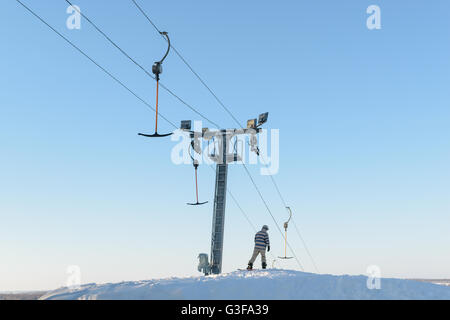 Snowboarder (sciatore) sorge vicino all'ascensore sulla cima di una collina ricoperta di neve e di preparazione per la discesa Foto Stock