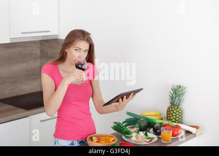 Giovane e bella ragazza guarda su un tablet ricetta per insalata. una cottura in cucina moderna. Uno stile di vita sano. Foto Stock