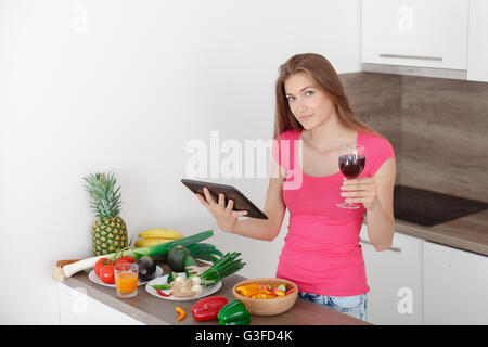 Giovane e bella ragazza guarda su un tablet ricetta per insalata. una cottura in cucina moderna. Uno stile di vita sano. Foto Stock