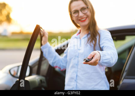 Giovane donna in piedi accanto a un auto con chiavi in mano - Concetto di acquisto di una macchina usata o un auto a noleggio Foto Stock