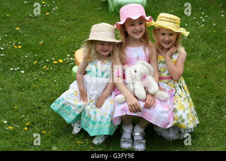 Le tre sorelle, bambini seduti in giardino a Pasqua indossando abiti di pasqua e la pasqua di cofani Foto Stock