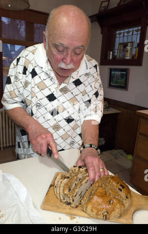 Uomo età 70 di tranciatura di un filone di soda tradizionale pane presso il giorno di San Patrizio festeggiamenti. St Paul Minnesota MN USA Foto Stock