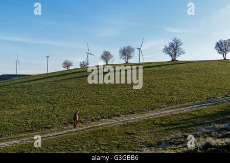 Uomo che cammina da sola in campagna con i mulini a vento vento in background, Ampudia, Palencia, Castilla y Leon, Spagna Foto Stock