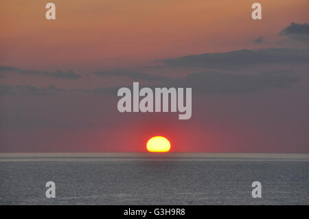 Cornwall - al tramonto - sun toccando orizzonte sul mare - rosso + arancio miscelatura - notte oscura le nuvole appaiono - riflessioni Foto Stock
