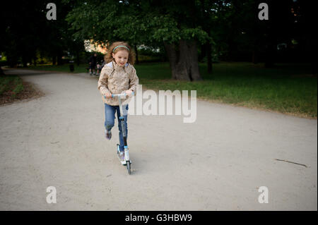 Il grazioso bambina corse scooter nel parco della città. Ragazza 7-8 anni felicemente portato sul suo scooter in pista. Il suo viso deligh Foto Stock