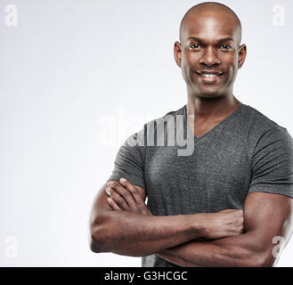 Unico bello montare grinning giovane adulto nero con la testa rasata e piegato bracci muscolare su uno sfondo grigio con spazio di copia Foto Stock