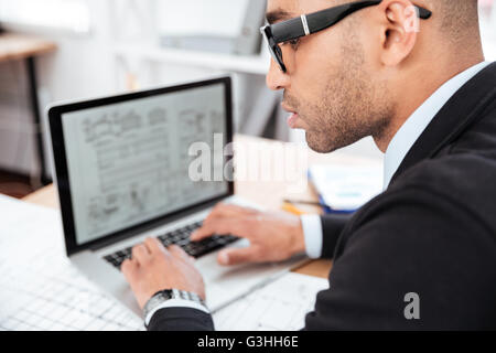 Close-up verticale di un imprenditore pensieroso a lavorare con il computer portatile in ufficio Foto Stock