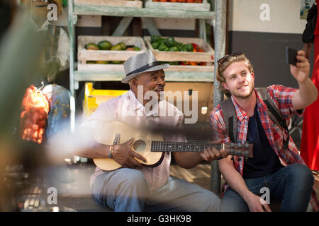 Turistica prendendo selfie con mercato trader giocando ukulele Foto Stock