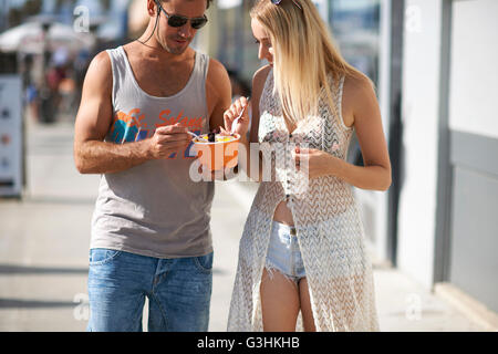 Paio di passeggiare e mangiare yogurt surgelato sul marciapiede, Venice Beach, California, Stati Uniti d'America Foto Stock