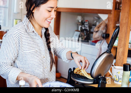 La donna in cucina waffle rimozione dalla piastra per i waffle sorridente Foto Stock