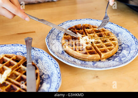 Vista ritagliata della mano womans diffondere il burro su cialde fresche Foto Stock