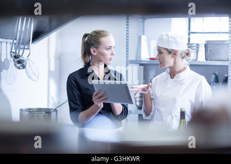 Cameriera e lo chef a discutere gli ordini sulla tavoletta digitale in cucina Foto Stock