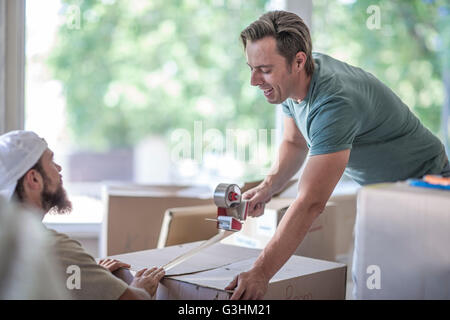 Casa in movimento: due uomini con nastro adesivo su una scatola di cartone Foto Stock