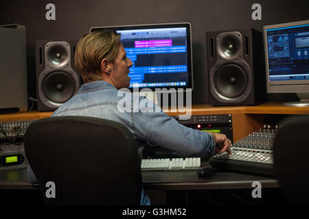 Uomo con miscelatore scrivania in studio di registrazione, vista posteriore Foto Stock