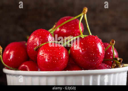 Fresche ciliege rosse in bianco coppa sopra rustico sfondo di legno Foto Stock