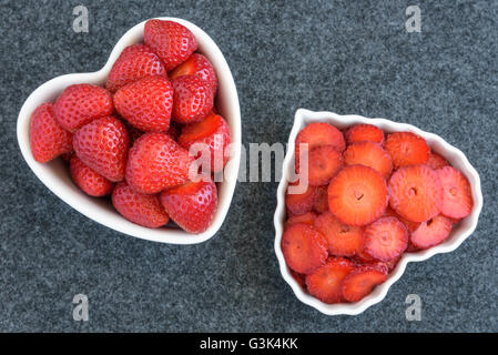 Intero e le fragole tagliate in due bianchi a forma di cuore ad bocce su sfondo nero Foto Stock