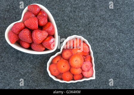 Intero e le fragole tagliate in due bianchi a forma di cuore ad bocce su sfondo nero Foto Stock