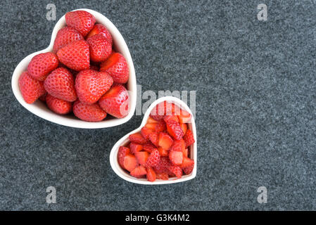 Intero e tagliate a dadini le fragole in due bianchi a forma di cuore ad bocce su sfondo nero Foto Stock