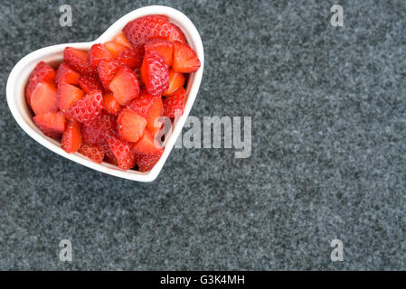 Tagliate a dadini le fragole in un cuore bianco ciotola sagomata su uno sfondo nero Foto Stock