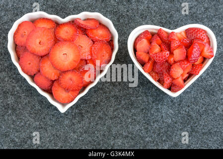 Affettate e tagliate a dadini le fragole in due bianchi a forma di cuore ad bocce su sfondo nero Foto Stock