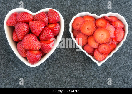 Intero e le fragole tagliate in due bianchi a forma di cuore ad bocce su sfondo nero Foto Stock