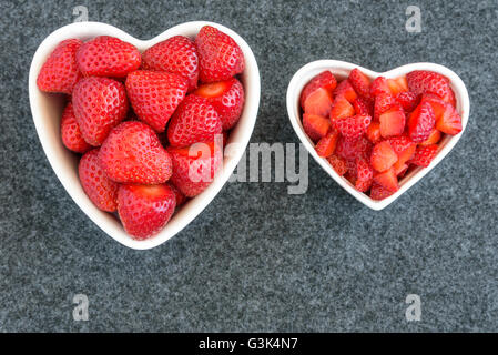 Intero e tagliate a dadini le fragole in due bianchi a forma di cuore ad bocce su sfondo nero Foto Stock