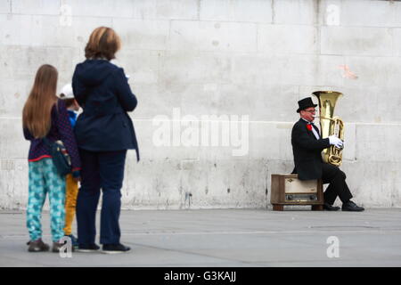 Un animatore di strada svolge una tuba in Trafalgar Square, Londra, guardato da una donna e due bambini. Foto Stock