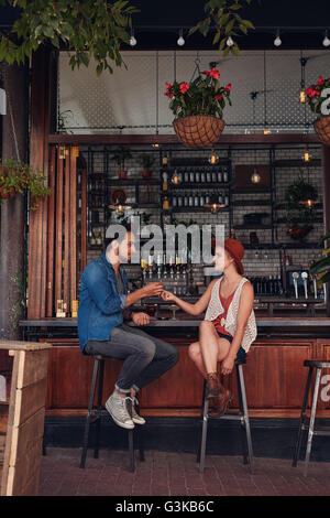 A piena lunghezza shot di coppia giovane seduto presso il cafe contatore. Giovane uomo e donna sigaretta condivisione presso la caffetteria. Foto Stock