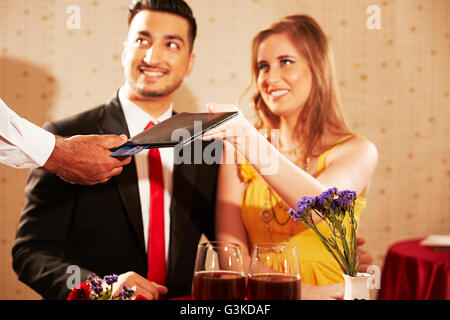 3 persone Le coppie sposate straniero e cameriere albergo cena dando le bollette Foto Stock