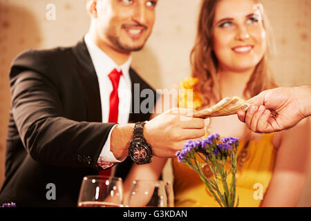 3 persone Le coppie sposate straniero e cameriere albergo cena dando le bollette Foto Stock
