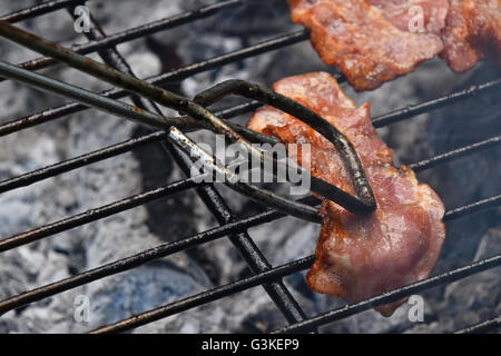 Pinze in azienda affumicato croccante grigliate barbecue fetta di pancetta, cotti sul fumo barbecue grill, close up Foto Stock