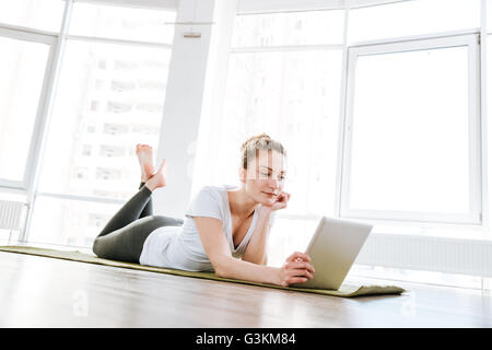 Bella giovane donna disteso sul materassino yoga e utilizzo di tablet in studio Foto Stock