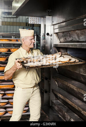 Felice baker ponendo il vassoio di fettine di pane nel forno Foto Stock