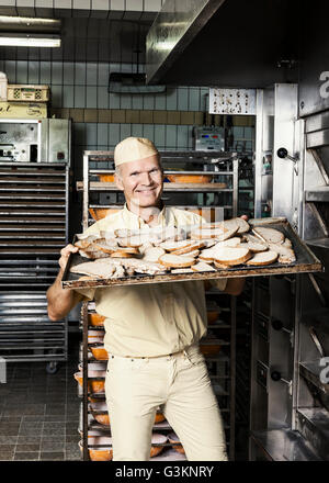 Felice baker ponendo il vassoio di fettine di pane nel forno Foto Stock