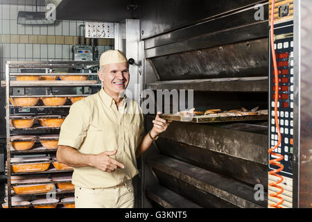 Felice baker ponendo il vassoio di fettine di pane nel forno Foto Stock