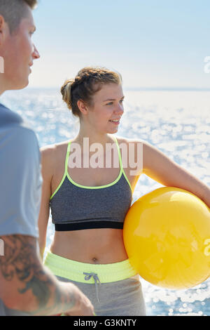 Donna di fronte oceano tenendo palla gialla che guarda lontano sorridente Foto Stock