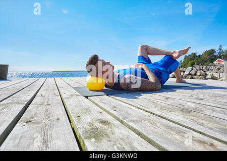 Tatuato uomo disteso sul molo con sfera come cuscino Foto Stock