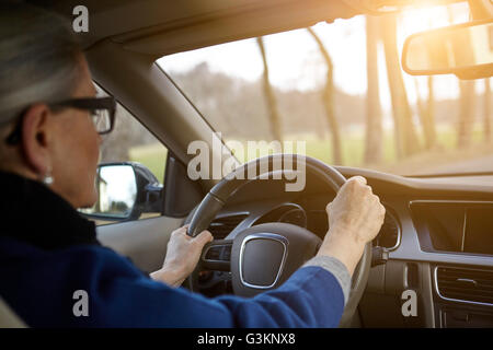 Al di sopra della spalla della donna in auto guidando su strada alberata Foto Stock