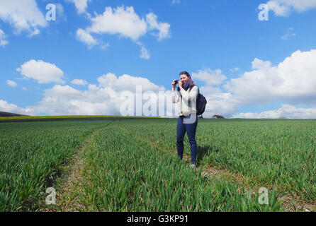 Giovane donna in piedi in campo, tenendo fotografia di paesaggio Foto Stock