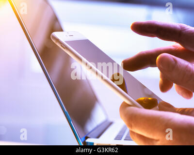 Uomo che utilizza un telefono cellulare con un computer portatile in background Foto Stock