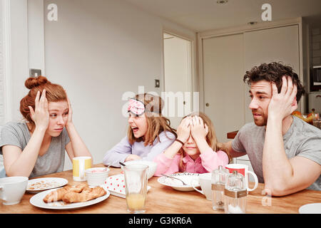 Stanco metà adulto genitori al tavolo per la colazione con due figlie Foto Stock